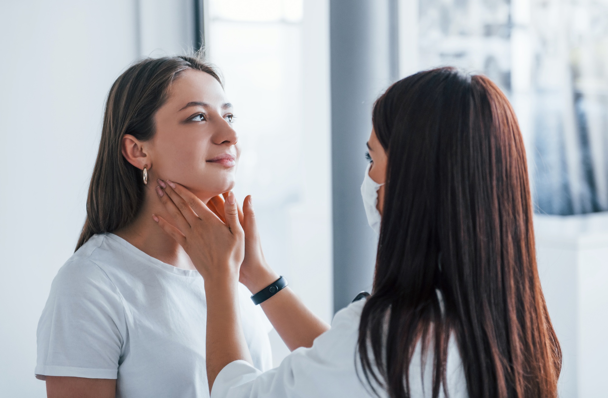 Checking lymph nodes and throat. Young woman have a visit with female doctor in modern clinic