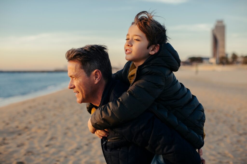 Father carrying son piggyback on the beach