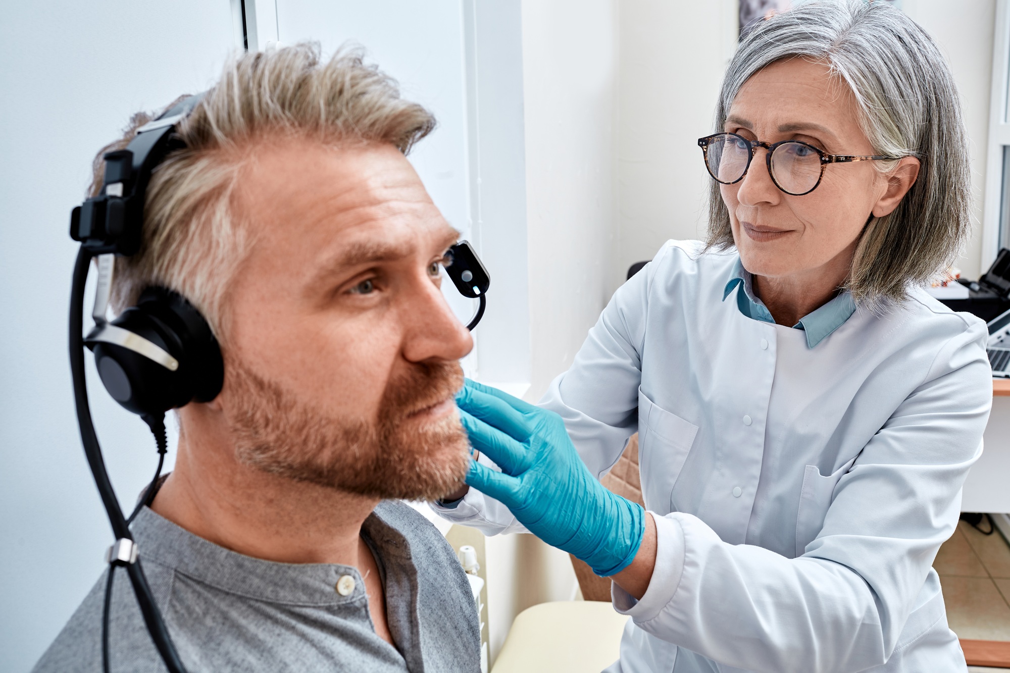 Mature man receives tympanometry with audiologist using tympanometer at audiology clinic. Hearing